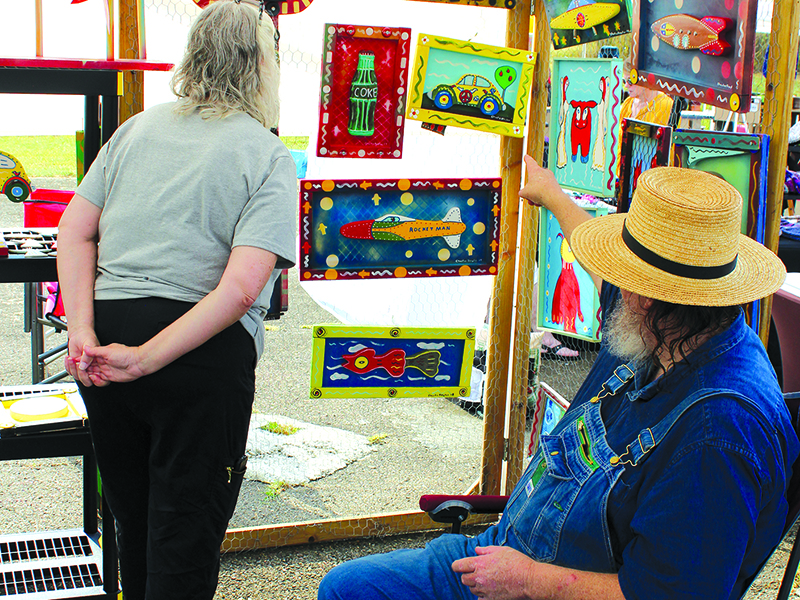 Charles Dingler shows Susan Catron, a Savannah resident and part-timer in Ellijay, one of his works of art at the Dancing Goats Folkfest.