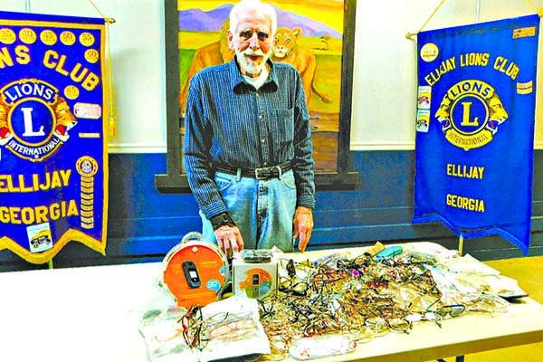 Lion Bill Leinmiller stands with donated eyeglasses and hearing aids collected for the Georgia Lighthouse Foundation.