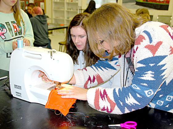 Ms. Andrea Handley teaches Stella Hegert how to use a sewing machine.