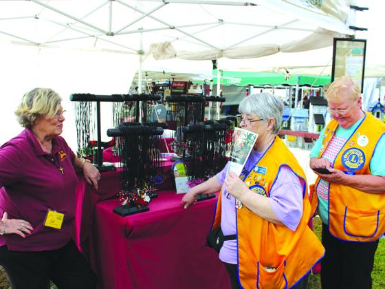 Proprietor Anne Bond, of Newnan, talks with regional Lions Club members Donna Calhoun (Chickamauga), left, and Jan Morris (Trion), about her Crosses from Nails booth just before the Apple Festival gates opened Saturday.