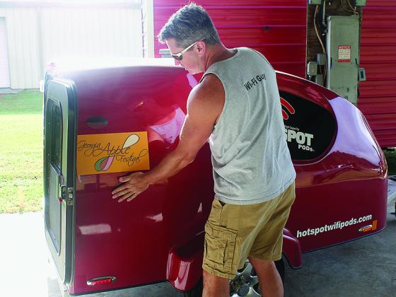 Bryan Baker, of Hot Spot Wi-Fi Pods, puts an official Apple Festival sticker on a mobile WI-FI hub that will allow improved payment processing for vendors at the 48th annual festival.
