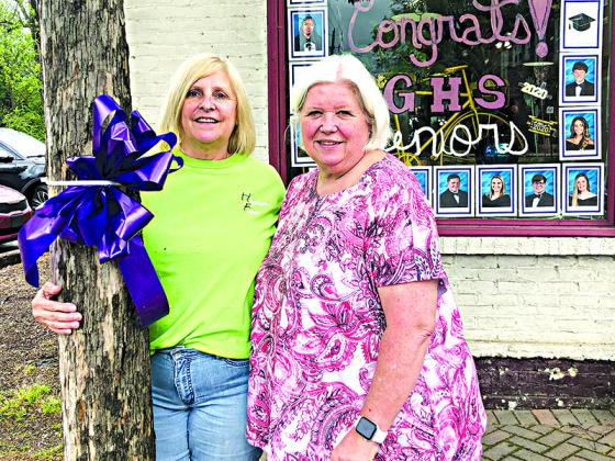 Judy Wilson, left, and Laura Thomas stand in front of Hometown Florist where a few senior portraits can be seen in the window.