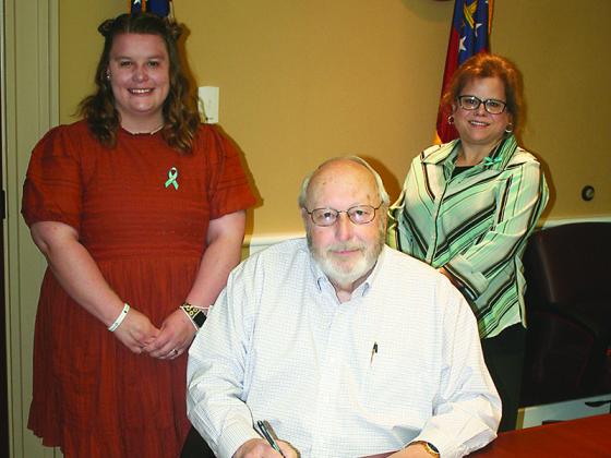 North Georgia Mountain Crisis Network representatives Julia Gilliam, left, and Kimberly O’Neal, right, join Gilmer Commission Chairman Charlie Paris for the signing of a proclamation that designates April as Sexual Assault Awareness Month in the county.