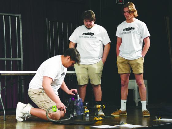 GHS student Tony Olea provides a cleaning demonstartion for a panel of judges during a Shark Tank-style presentation as business parners Alexis Martinez and Spencer Merritt observe.