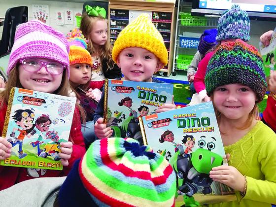School children happily show new books and hand-knitted hats they received as part of a previous delivery by the Craddock Center.