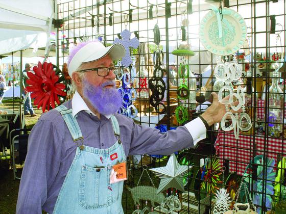 Colorful Apple Festival vendor John Padgett explains the inspiration behind some of the wind chimes made by him and wife, Evelyn. Padgett dyes his beard a different color for every event they attend.