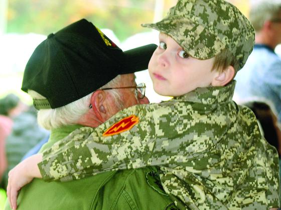 Young Luke Kerr gets a lift from his grandpa, Vietnam veteran Harold Henson, as they watch the honorary Veterans Day program at the Lions Club Pavilion. 