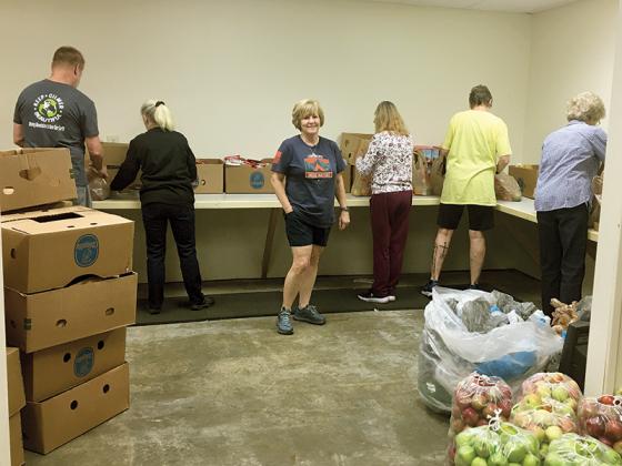 Members of the Gilmer Community Food Pantry Sack Pack team, led by volunteer Lu Hale, facing, work to bag weekend food for more than 300 local children.