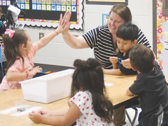 Teaching assistant Melissa Long high-fives Trinity Dazey and helps Jayden Morales Lorenzo make his friendship bracelet in Laura Bramlett’s kindergarten class.