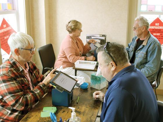 Poll worker Jackie Watson checks in Martin Wintermantel in the foreground while Nancy Vandiver gets Vernard Turner ready to cast his vote during the first day of early voting in Gilmer County, Oct. 15.