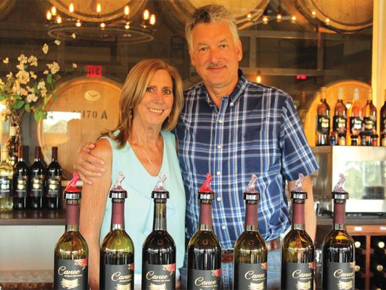 Charles and Cathy Hoetink, owners and proprietors of Canoe Vineyards & Winery, pose with their collection of wines for tasting and purchasing. Charles is from the Netherlands, and Cathy hails from Memphis, Tenn. (Photo by Mark Millican)
