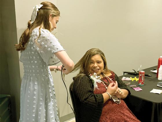 Cosmetology student and volunteer Lilly Penland helps honored guest Natalie Ledesma straighten her hair at the beauty station.