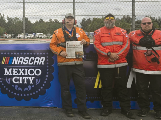 Max Frady, of Ellijay, third from right, holds up an issue of the Times-Courier at the recent NASCAR Cup Series Race at Mexico City. Members of the Race Recovery Team, one of several at the event, are tow operators from around the country. 