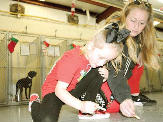 Ella Rhodes, left, and her mom, Caroline Rhodes, right, write a cheery Christmas message for the dogs in the Gilmer County Animal Shelter Monday, Dec. 22.