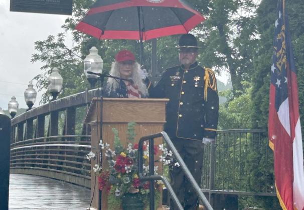 Gold Star Mother Lucy Wheeler, left, speaks for the dedication of the Gilmer Veterans Memorial Wall on Monday, May 25, as Sheriff’s Honor Guard member Jeff Ellington, right, holds her umbrella.