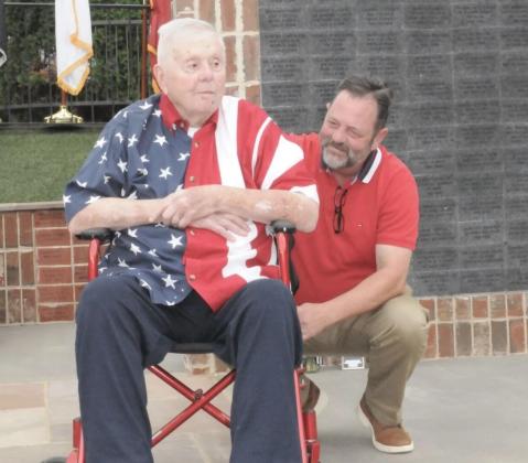Air Force Staff Sergeant Sandy Lyons, the creator of the original Veterans Memorial Bridge, left, receives recognition for his work honoring Gilmer Veterans at the Gilmer Veterans Memorial Wall Dedication Monday, May 25. He is accompanied by his son, Andrew Lyons, right.