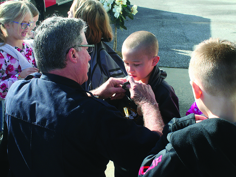 Firefighter Jeff Statham pins a junior fire chief badge onto Nolan Tatum, one of the local second graders who completed the Ellijay Fire Department’s safety and prevention course this year.