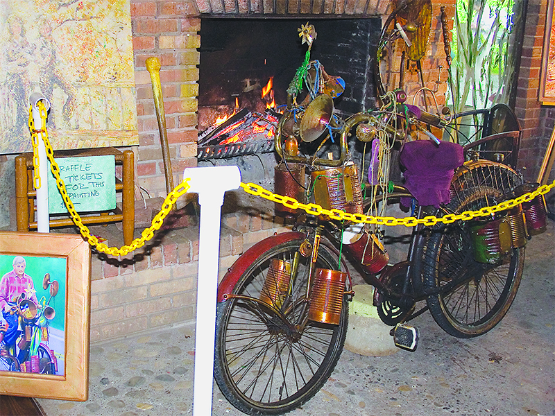 The uniquely outfitted bicycle once ridden by the late RT Henson will be on display at the Gilmer Chamber’s Downtown Ellijay Welcome Center from Oct. 11-20. The lacquered bike is seen above next to a painting of Henson by artist Daniel Norris during a 2009 public tour of the artist and inventor’s equally unique Ellijay home.