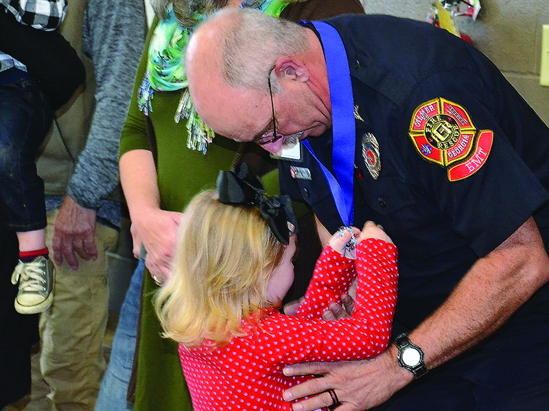 Retiring firefighter/EMT Mike Sales’ granddaughter, Hayden, gets an up-close look at the Medal of Honor her grandpa was awarded during a recent Gilmer Fire and Rescue ceremony that marked Sales’ 40 years of employment with the county public safety agency. 
