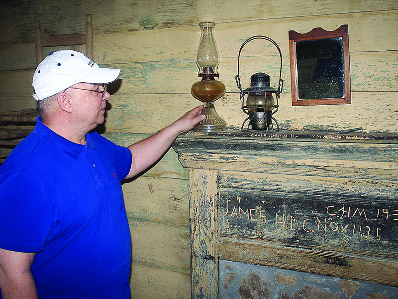 Wayne Hooper places a kerosene lamp on a fireplace mantel in one of the exhibit rooms at the Gilmer Historical Society’s Tabor House Museum. The inscription on the mantel, believed to have been made when the oldest standing home in downtown Ellijay was used as a boarding house, is dated 1936.