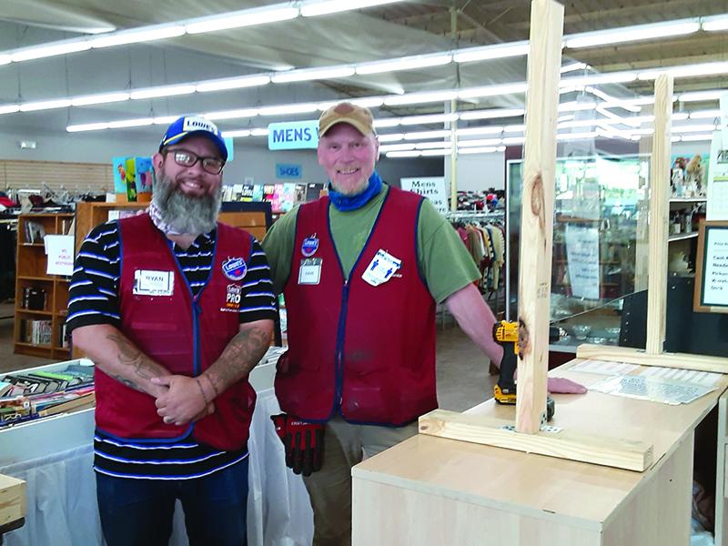 Ryan Harper and Dave Hankison, both of the East Ellijay Lowe’s, install one of two protective sneeze guards now in place at the checkout area of Faith, Hope and Charity Recycle Store.