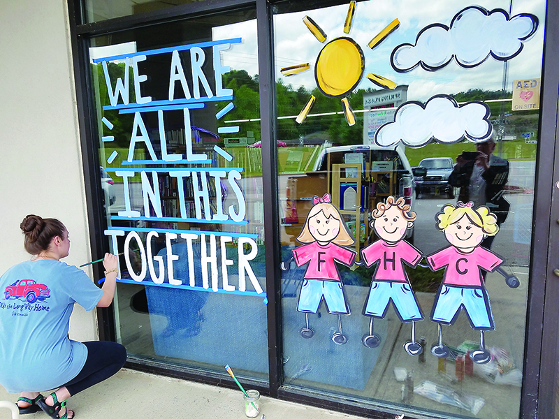 Dotson puts the finishing touches on a mural and positive message in the window of Faith, Hope and Charity Recycle Store. 