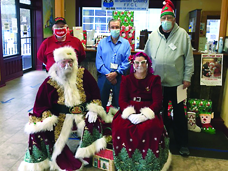 Volunteers at the Gilmer Community Food Pantry gather with special guests for the food pantry’s first Christmas event for families. Pictured, from left, back: Jim Adams of Gilmer Toys For Tots, food pantry director Allen Triebel and food pantry volunteer Paul Bryant; front: Semper Fi Santa (Jon Vigue) and Mrs. Semper Fi Santa (Michelle Vigue). 
