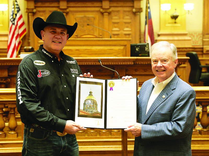 At the Georgia State Capitol, Roger Mooney, left, and Sen. John Wilkinson hold a framed copy of Senate Resolution 951, which honors Mooney’s 36-year career as a professional rodeo announcer.