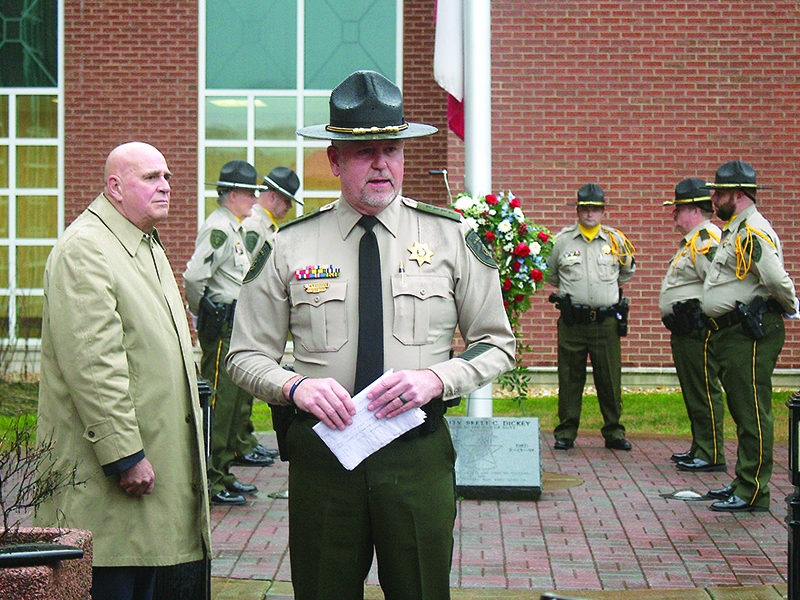 On a rainy Saturday morning, Gilmer County Sheriff Stacy Nicholson speaks to attendees at a 25th anniversary memorial service for Deputy Brett Dickey, killed in the line of duty Feb. 13, 1996. Pictured, at left, is sheriff’s office chaplain Scotty Davis. Gathered around a wreath placed at a memorial marker for Dickey outside the Gilmer County Courthouse are Cpl. Al Greenway, Cpl. Randy Beavers, Deputy Josh Easley (obscured), Sgt. Gene Hefner, Capt. Brian Crump and Deputy Josh Chancey.