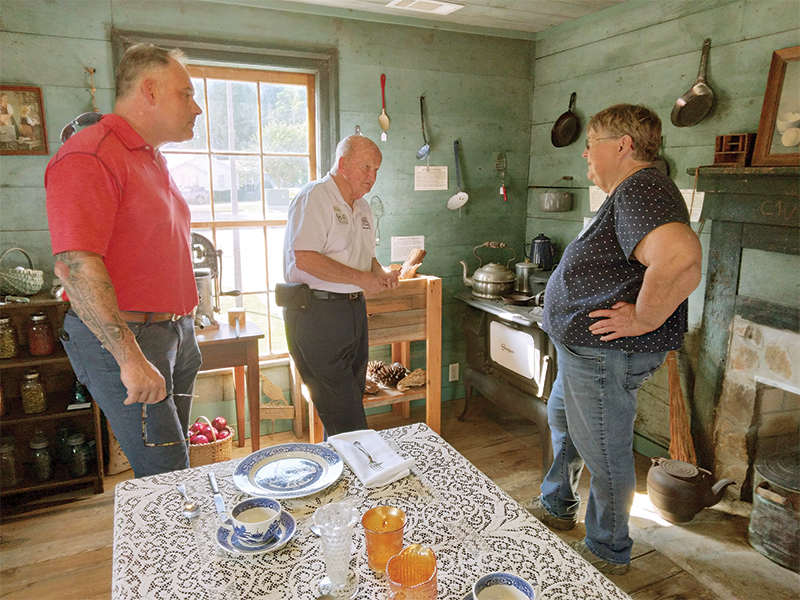 Ron Cheslock, left, and Joe Sewell, center, both of the Gilmer Chamber, get a tour of the Tabor House Museum’s old-fashioned southern kitchen display from museum volunteer Pam Johnson.