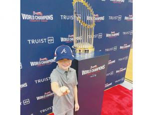 Ellijay’s Zane Johnson proudly stands next to the Braves 2021 World Series trophy at the Gilmer High School gym Sunday. Around 500 people stopped by throughout the day to get a glimpse and photo with the Braves first World Series trophy since 1995.