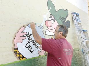 Artist John Christian paints Willy the Hillbilly, part of a throwback Mountain Dew mural on the side of the building at 24 River Street.  